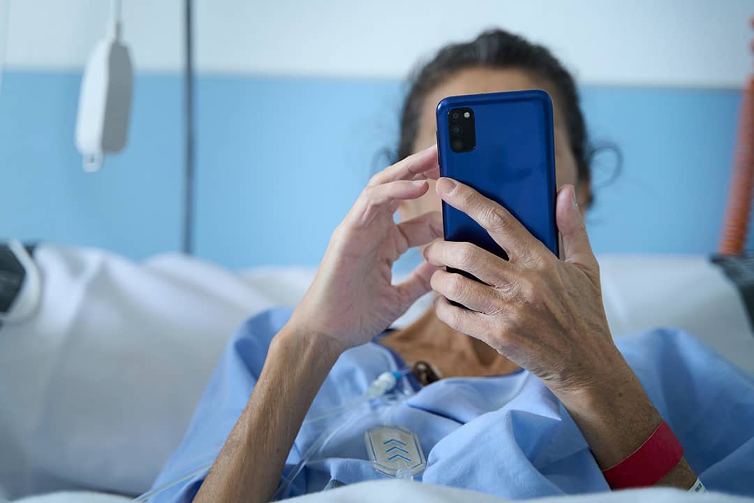 An elderly woman in a hospital bed checking her smartphone.
